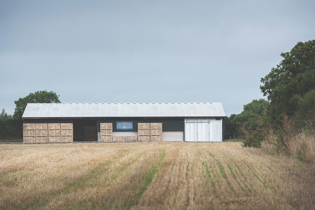 A barn for processing and storing firewood sits alongside a field. 
